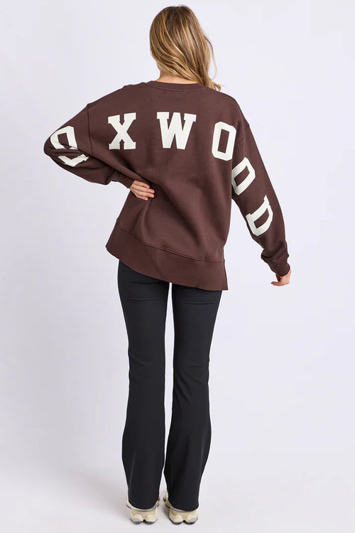 Person wearing a brown sweatshirt with 'OXWOOD' text on the back, standing against a white background.