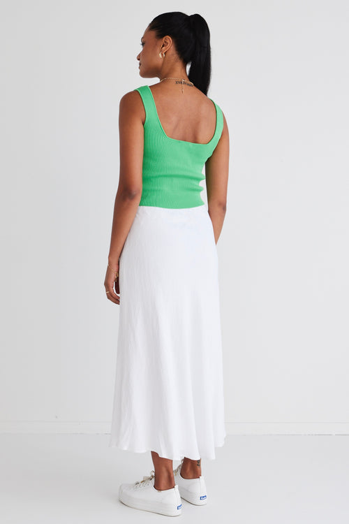 model wears a green top and white linen skirt