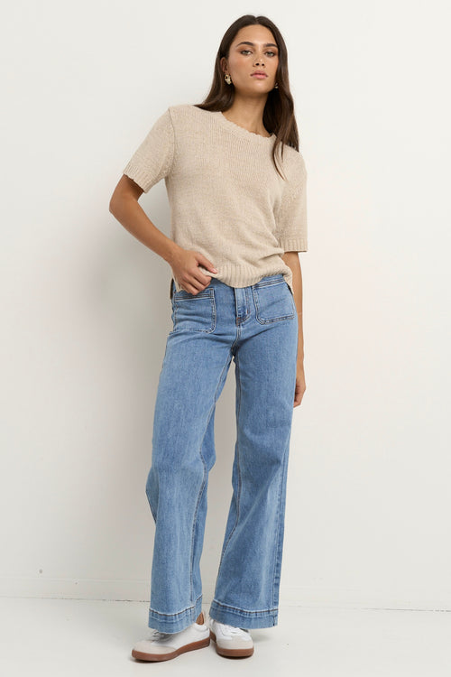 Woman wearing a short sleeve natural-toned knit top with ribbed edges and light blue jeans.