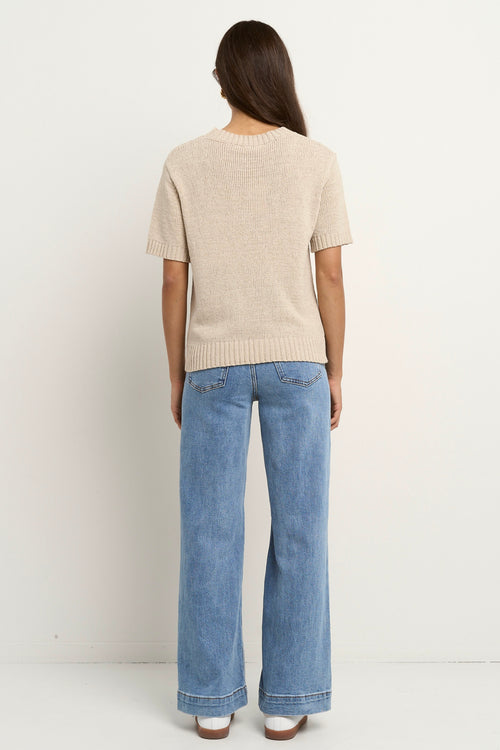 Woman wearing a short sleeve natural-toned knit top with ribbed edges and light blue jeans.