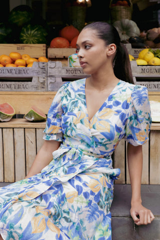 model wears and blue and orange floral maxi dress in front of a fruit stall