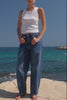 Woman standing on rocks by the ocean wearing a white top and blue jeans.