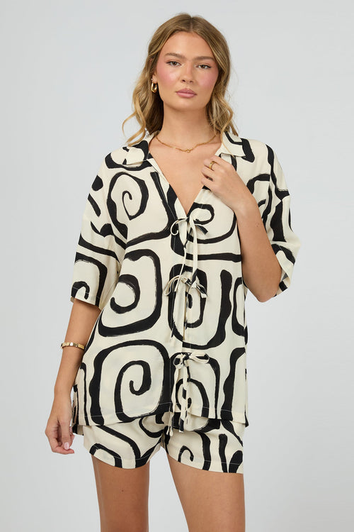 cream buttonless shirt with bold black swirl print and multiple front tie fastenings, worn with gold jewellery