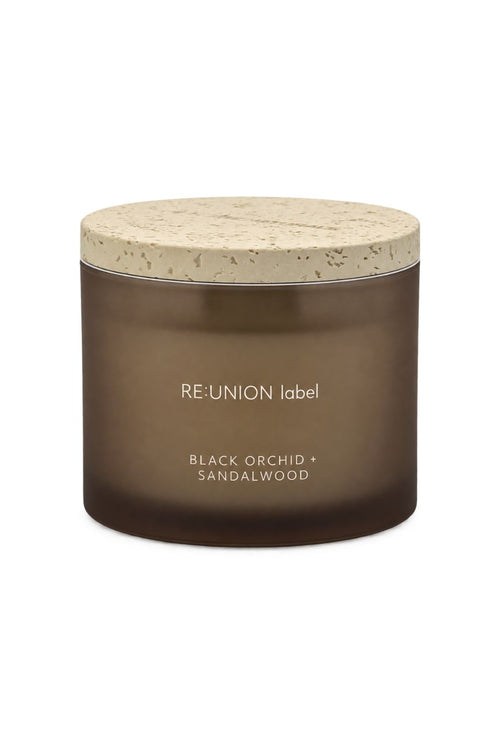 A dark brown glass jar candle with a light beige textured stone-look lid, labeled 'RE:UNION label BLACK ORCHID + SANDALWOOD' on a white background.