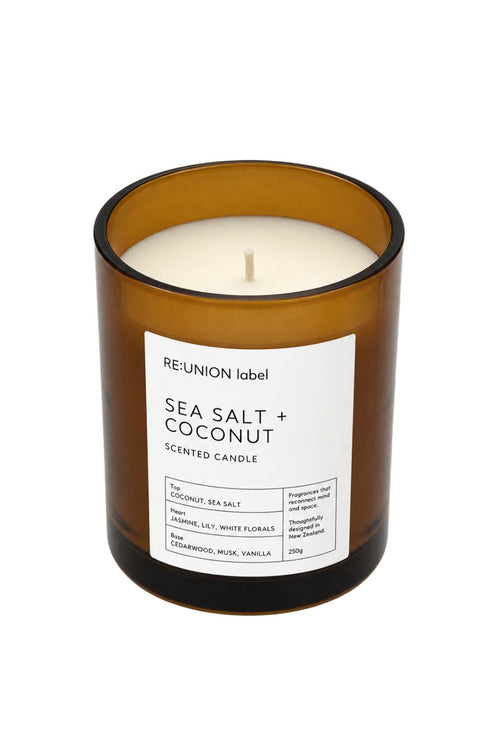 An amber glass jar candle with a white label reading 'RE:UNION label SEA SALT + COCONUT SCENTED CANDLE' on a plain white background.