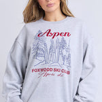 Woman wearing a gray sweatshirt with 'Aspen Foxwood Ski Club' text and graphics on a light gray background