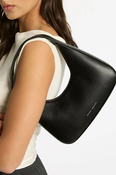 Model wears a black leather shoulder bag by brand status anxiety