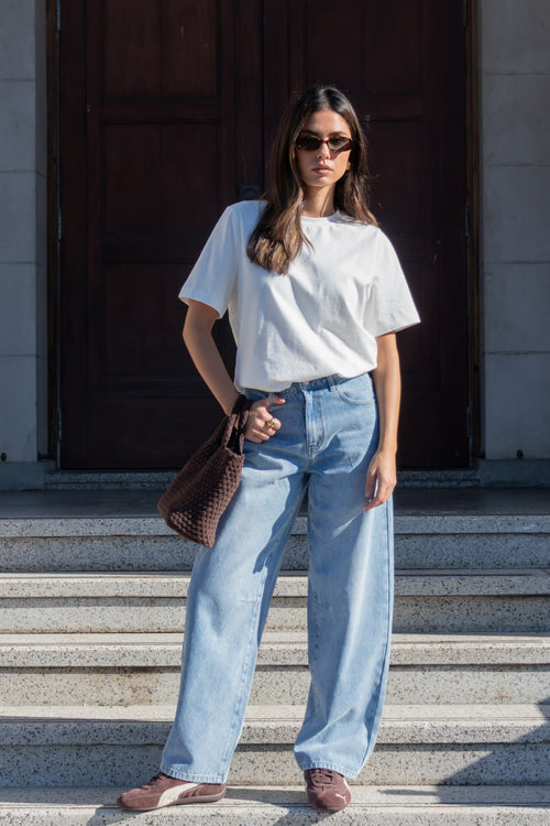 Woman in white t-shirt and light blue jeans standing on stone steps.