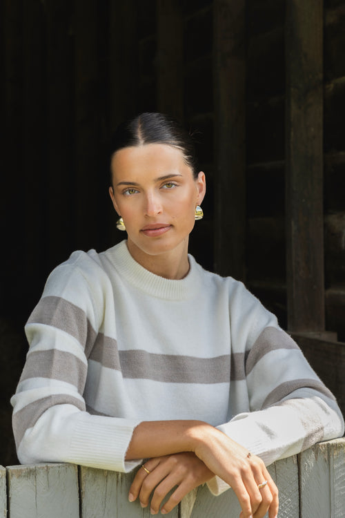 A cosy natural and taupe striped crewneck sweater styled with blue denim, creating a relaxed yet refined everyday look.