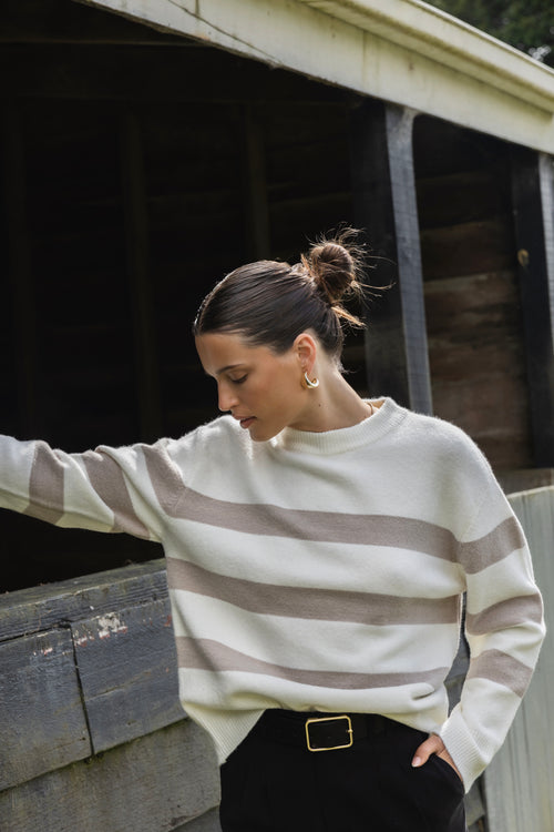 A cosy natural and taupe striped crewneck sweater styled with blue denim, creating a relaxed yet refined everyday look.