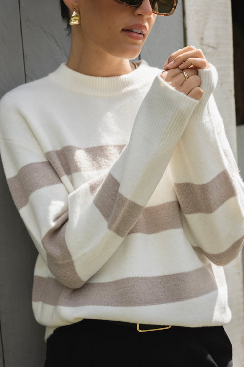 A cosy natural and taupe striped crewneck sweater styled with blue denim, creating a relaxed yet refined everyday look.