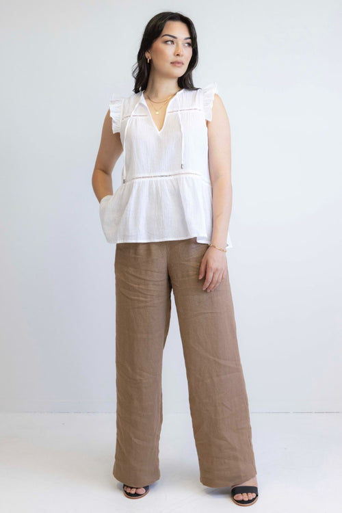 model wears white sleeveless top with brown pants